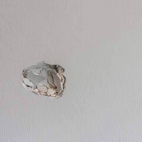 A wall with textured paint finish that has a crushed hole knocked into the drywall